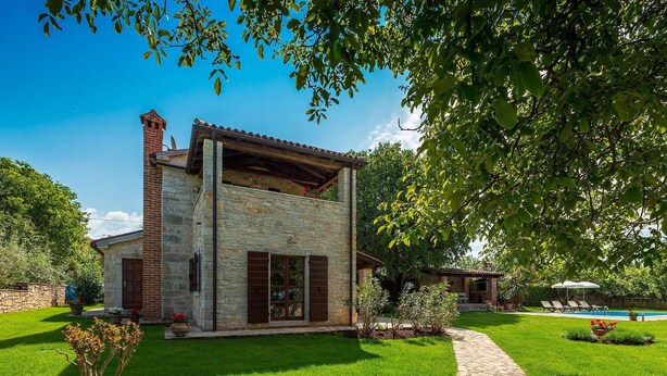 Una casa de piedra con balcón de madera, piscina y jardín bien cuidado.