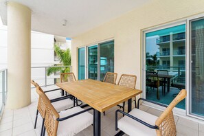 Una mesa de madera con seis sillas, un balcón con barandilla y vistas a un edificio con balcones.