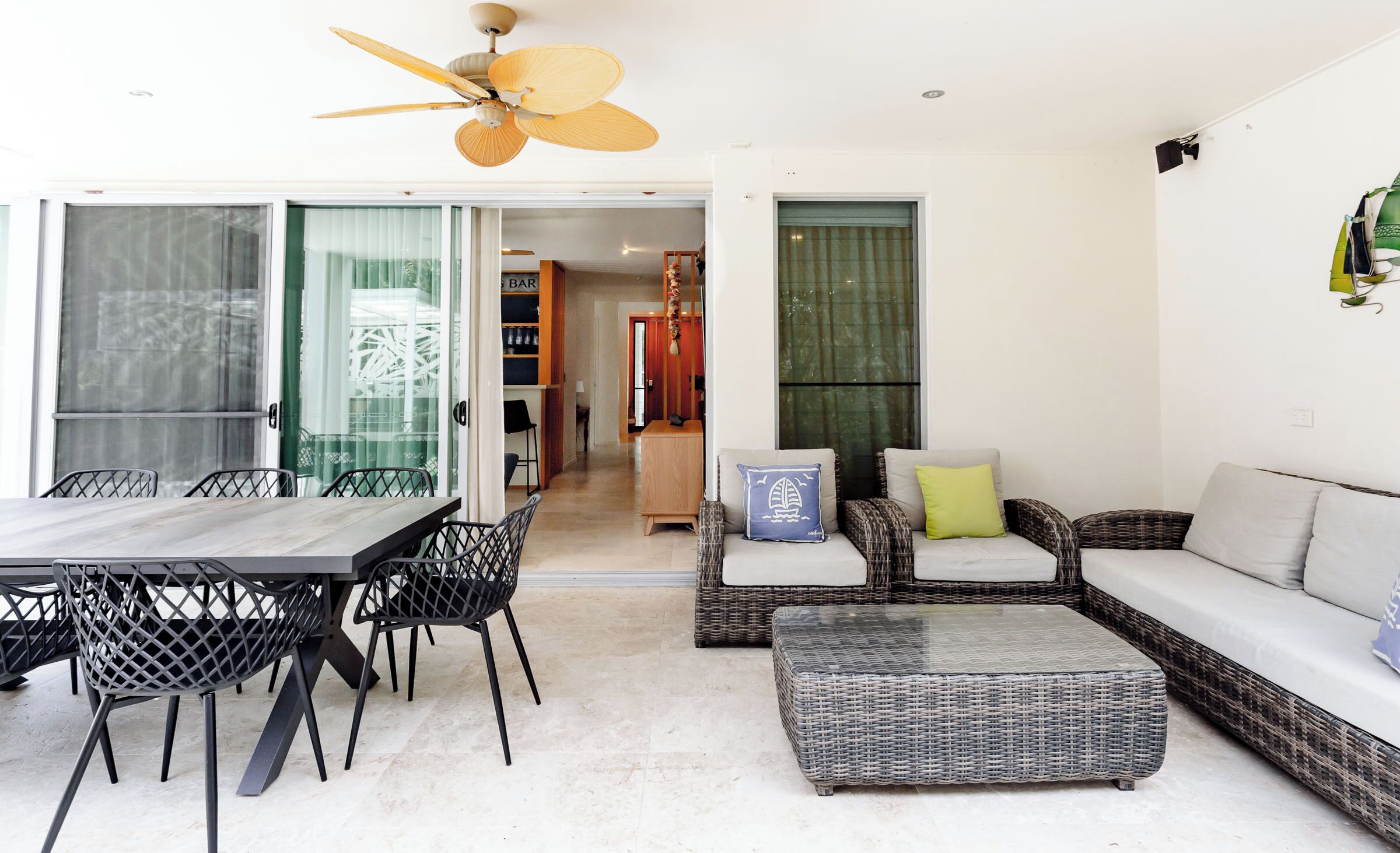 A modern living room with a dining area, wicker furniture, and a ceiling fan.