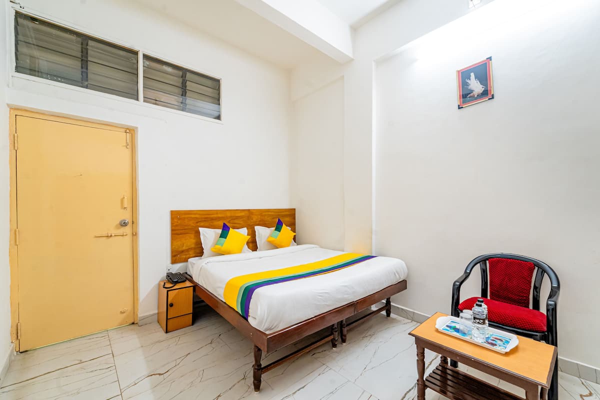 A neatly arranged hotel room with a wooden bed, a small bedside table, a chair, and a door.