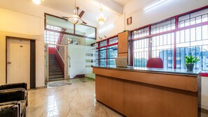 A reception area with a wooden desk, a laptop, a red chair, a potted plant, and a staircase leading to an upper floor. - Itsy Hotels Mansi (Nashik)