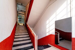 A staircase with red and white walls, a marble floor, and a metal railing. - Itsy Hotels Mansi (Nashik)
