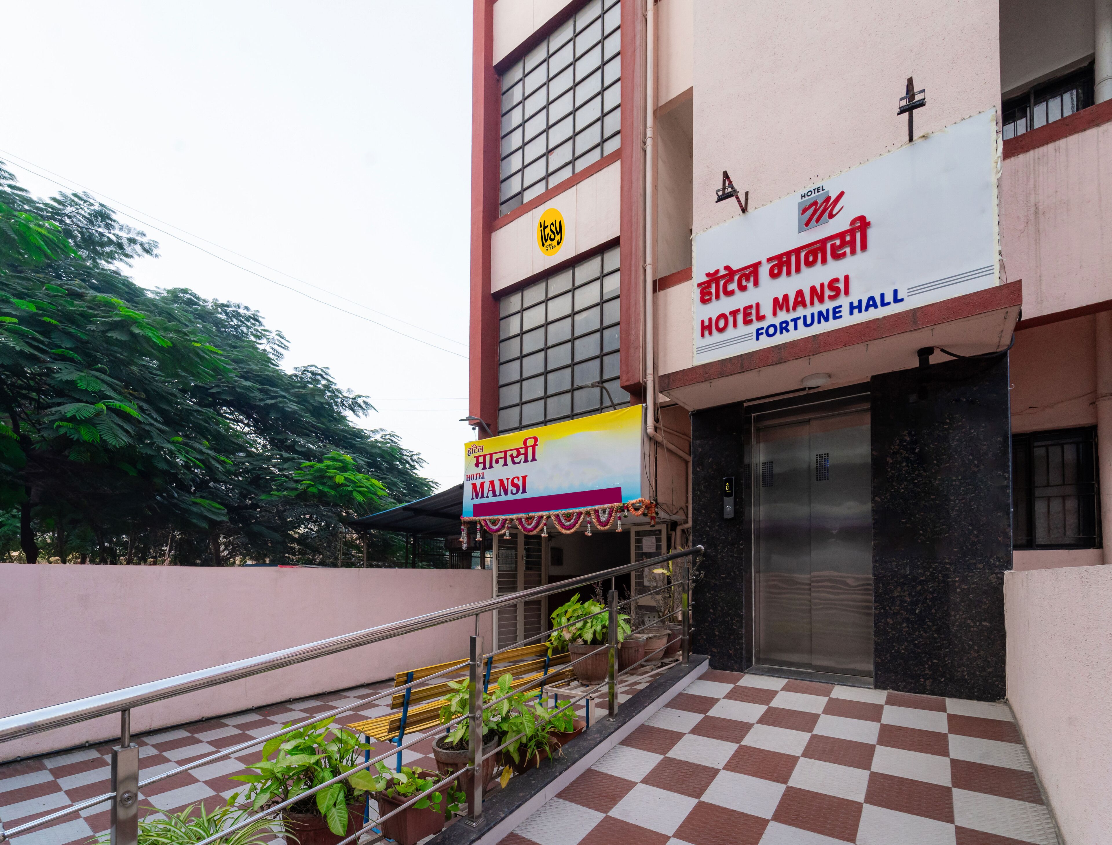 Entrada de hotel com chão quadriculado, escada e plantas em vasos.
