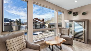 A spacious living area with large windows, a wooden coffee table, and a modern kitchen with a refrigerator. - 200cdk5 (Keystone)