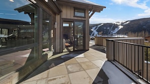 A modern building with large glass windows, a balcony with a metal railing, and a view of a snowy mountain landscape. - 200cdk5 (Keystone)