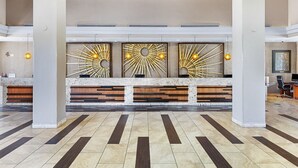 A spacious lobby with a reception desk, modern art installations, and a tiled floor.