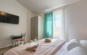 A hotel room with a bed, a desk with a chair, a TV mounted on the wall, and a window with curtains. - Amazing home in Zminj with sauna (Zminj)