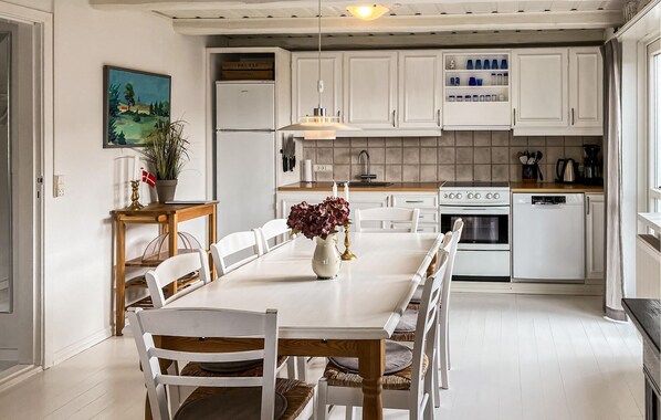 A kitchen with white cabinets, a dining table with chairs, a stove, and a refrigerator.
