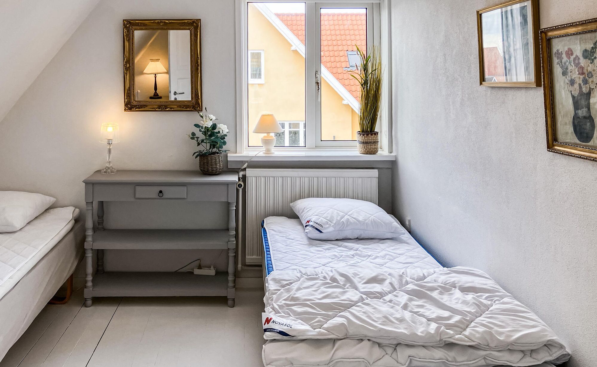 Ein Schlafzimmer mit Bett, Schreibtisch, Heizkörper, Fenster und Spiegel.