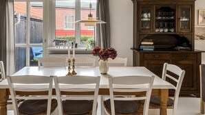 En spiseplads med et hvidt bord og stole, en vase med blomster og et træskab med glas.