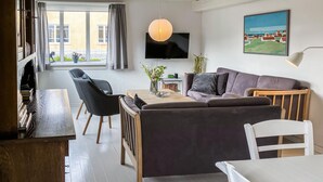 En moderne stue med sofa, stole, sofabord, fjernsyn og et billede på væggen.
