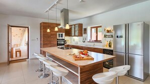 A modern kitchen with a central island, bar stools, stainless steel appliances, and wooden cabinetry. - Pet friendly home in Tinjan (Tinjan)