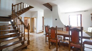 Una habitación amplia con una escalera de madera, un comedor con sillas de madera y un gran ventanal que proporciona luz natural.