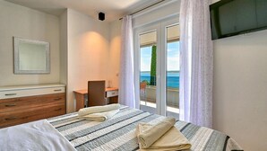 Ein Schlafzimmer mit Bett, Schreibtisch, Stuhl und Meerblick durch eine Schiebetür.