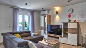 Ein modernes Wohnzimmer mit grauem Sofa, Couchtisch, Flachbildfernseher und einer Vitrine.