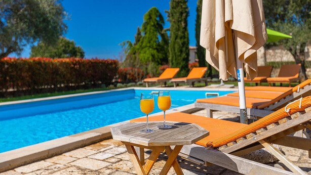 Area piscina con lettini e un tavolo con due bicchieri di succo d'arancia.