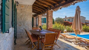 Un'area pranzo all'aperto riparata, con un muro in pietra, un tavolo e sedie in legno.