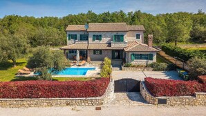Una casa in pietra su due piani con piscina, immersa nel verde e circondata da un muro in pietra.