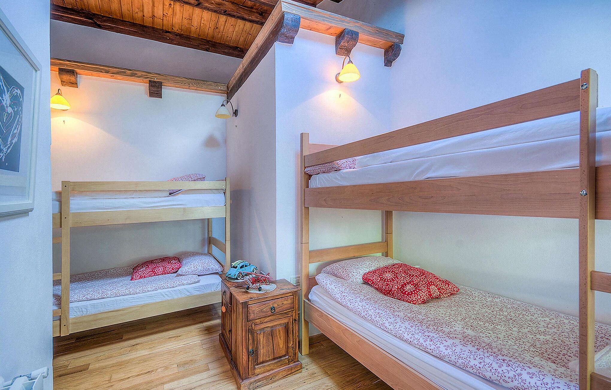 Ein Schlafsaalzimmer mit zwei Etagenbetten, Holzböden und einem kleinen Nachttisch aus Holz.