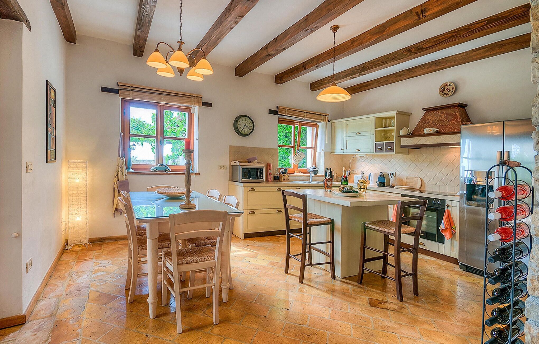 A kitchen with a central island, wooden beams, stone flooring, and a wine rack.