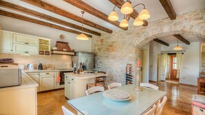 Una cocina rústica con paredes de piedra, vigas de madera y un comedor con mesa de vidrio.