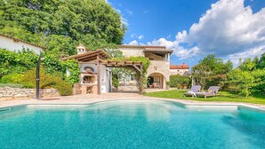 Una piscina con un patio de piedra, una pérgola y un edificio de piedra con techo rojo.