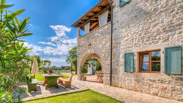 Un edificio de piedra con patio, mesas al aire libre y vistas del paisaje circundante.
