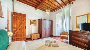 A bedroom with a wooden ceiling, a wardrobe, a wicker chair, a dresser, and a bed with a green pillow. - 2 bedroom nice home in Follonica (Follonica)