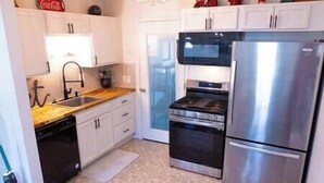 Una cocina compacta con gabinetes blancos, un refrigerador de acero inoxidable y una estufa negra.
