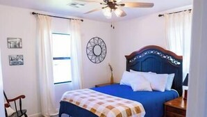 Un dormitorio con cama, una mecedora de madera, un ventilador de techo y un reloj de pared.