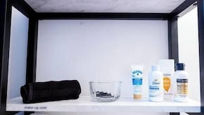 Una estantería con una toalla negra, un recipiente de vidrio y tres botellas de artículos de aseo.