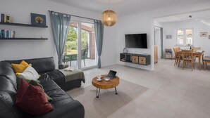 A modern living room with a black leather sofa, a round wooden coffee table, and a TV mounted on the wall. - Awesome home in Buzinija with private swimming pool, can be inside or outside (Buzinija)