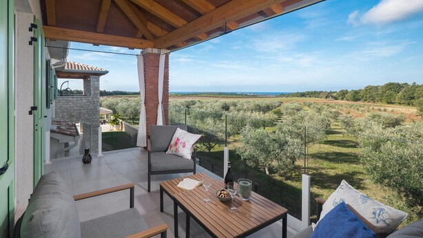 A balcony with a stone wall, a wooden table, two chairs, and a view of olive groves. - Awesome home in Buzinija with private swimming pool, can be inside or outside (Buzinija)