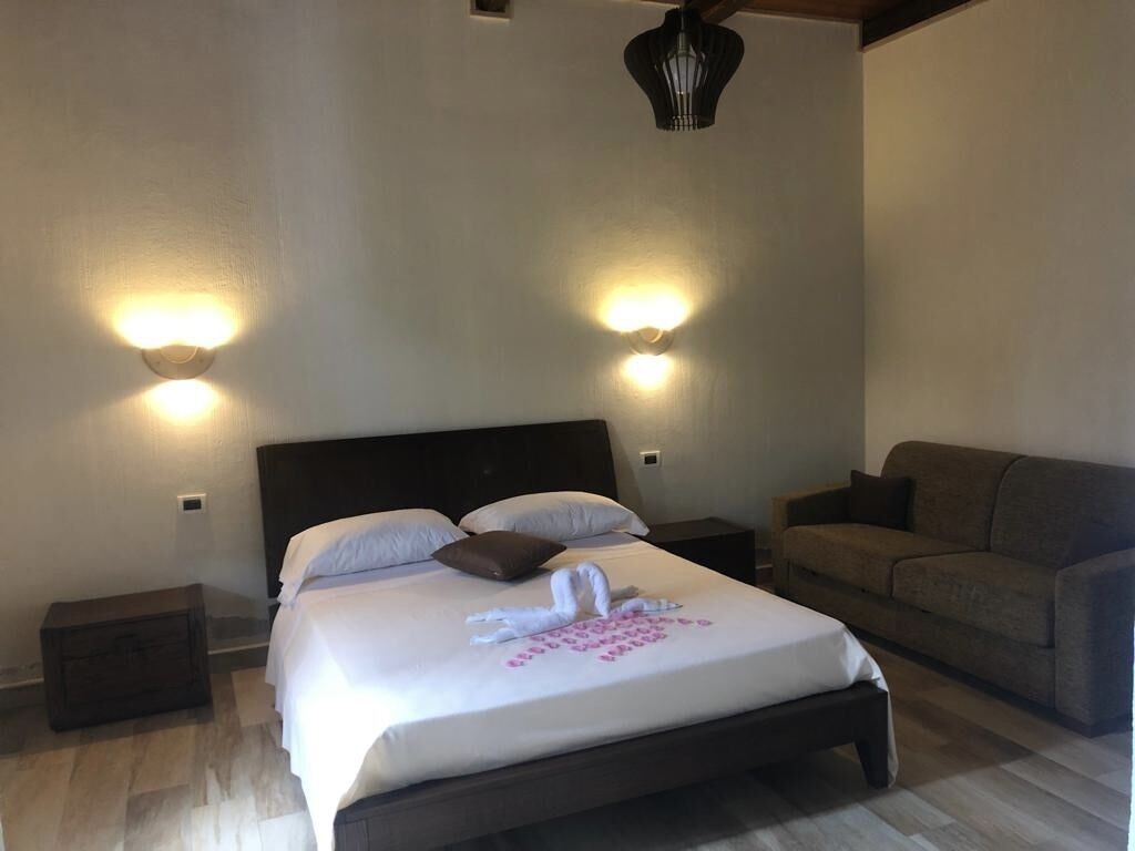 A neatly made bed with a swan and rose design, two bedside tables, a sofa, and wall-mounted lights.