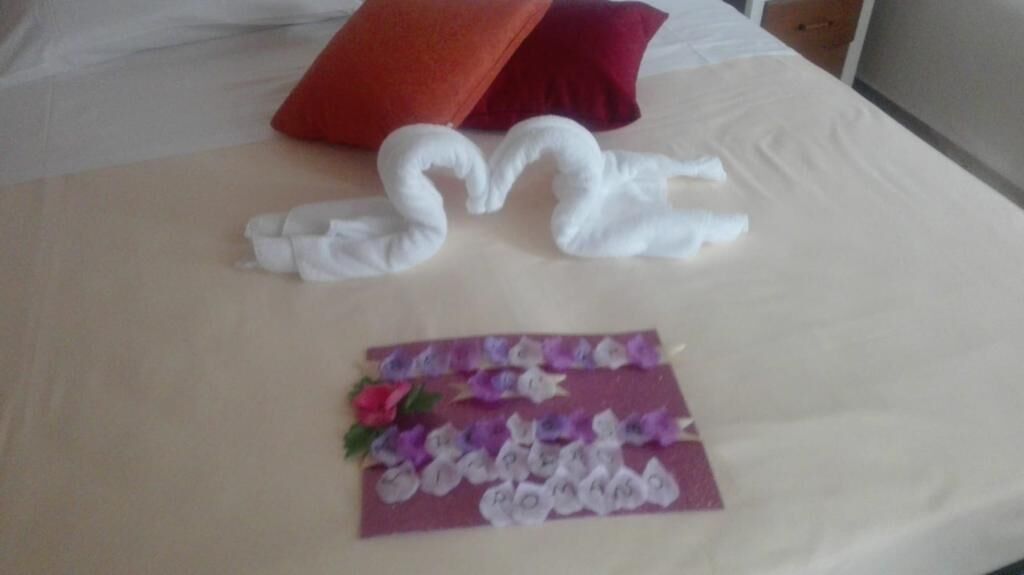 Una cama bien hecha con un diseño de toalla con forma de cisne y una tarjeta decorativa con flores.