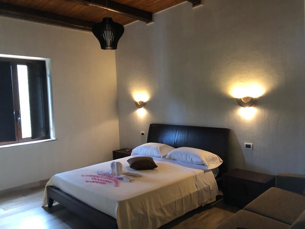 Un dormitorio con cama, mesitas de noche, ventana e iluminación en la pared.