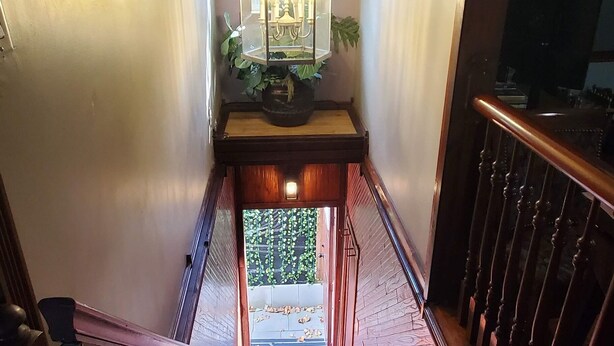 A wooden staircase with a railing, leading to a landing with a chandelier and a potted plant. - Beautiful 1 Bedroom Loft with big jetted tub and shower also on-site parking ! (Indianapolis)