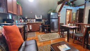 A cozy living room with a sofa, a coffee table, and a dining area with a table and chairs. There's a kitchen area with a refrigerator, microwave, and stove. - Beautiful 1 Bedroom Loft with big jetted tub and shower also on-site parking ! (Indianapolis)