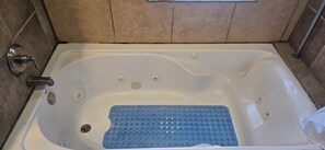 A bathtub with a blue mat, a faucet, and a drain.
