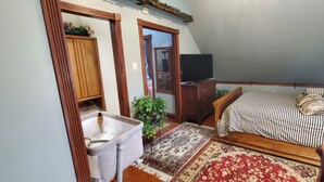 A bedroom with a bed, a wooden wardrobe, a television, and a small plant. - Beautiful 1 Bedroom Loft with big jetted tub and shower also on-site parking ! (Indianapolis)