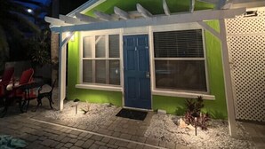 Une petite maison avec une porte bleue, un porche abrité et un patio aménagé avec des chaises et des plantes.