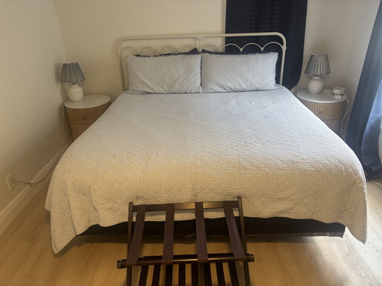 Een bed met een gestreept dekbedovertrek, twee nachtkastjes met lampen, een houten stoel en een raam met gordijnen.