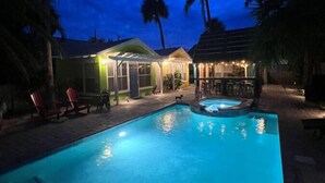 A swimming pool with lounge chairs and a bar area, surrounded by palm trees and a building with outdoor lighting.