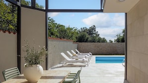 A poolside area with lounge chairs and a table, a potted plant, and a stone wall. - Villa Pietra Cattunara (Brtonigla)