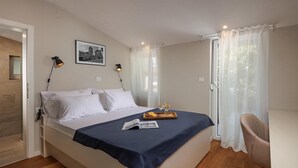 A neatly made bed with white linens and a dark blue bedspread, two bedside lamps, a framed picture on the wall, and a tray with glasses and snacks on the bed. - Villa Pietra Cattunara (Brtonigla)