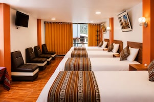 Une chambre d’hôtel avec deux lits, un coin salon avec des fauteuils, une télévision et une fenêtre avec des rideaux.