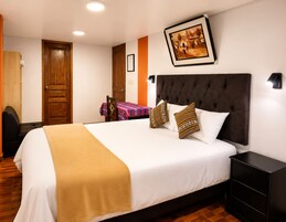 Habitación de hotel con una cama grande, una mesita de noche, una puerta de madera y un cuadro en la pared.