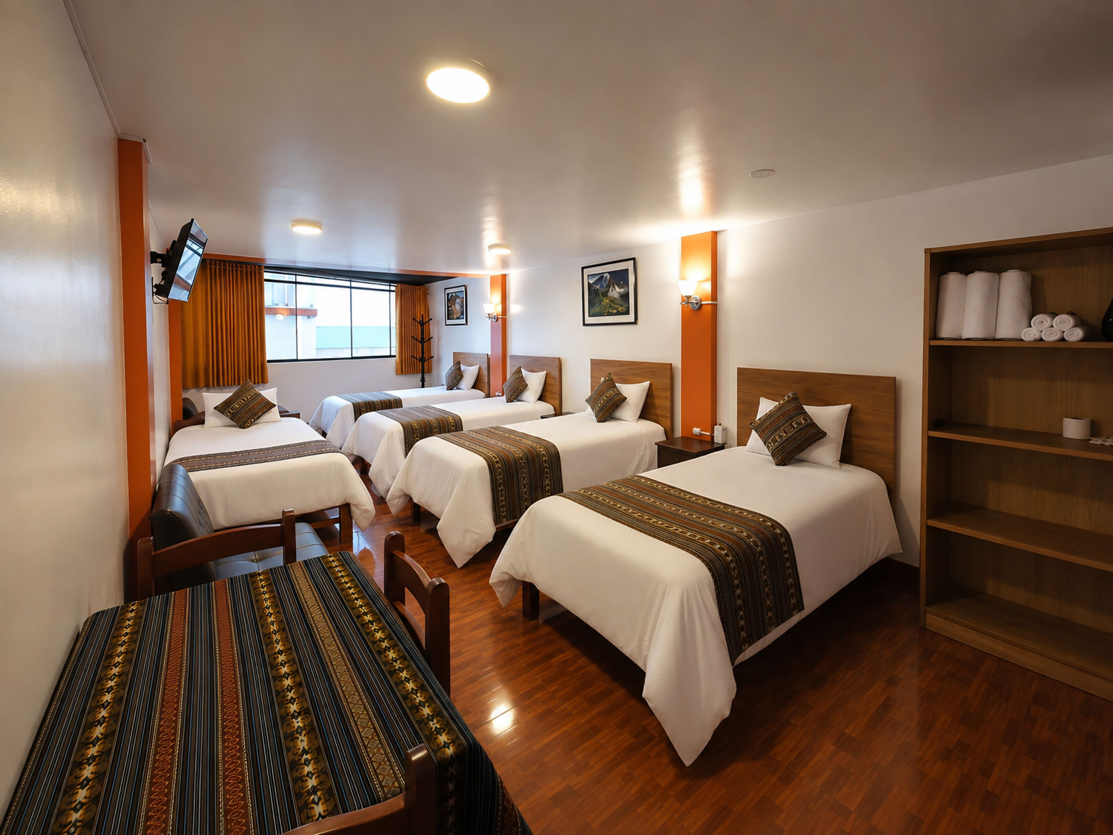 Habitación de hotel con cuatro camas, una mesa de madera y una estantería con toallas.