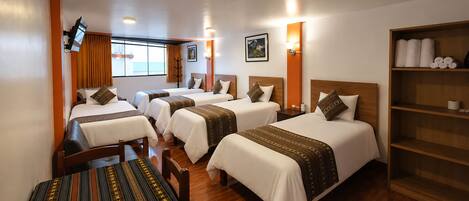Habitación de hotel con cuatro camas, una mesa de madera y una estantería con toallas.