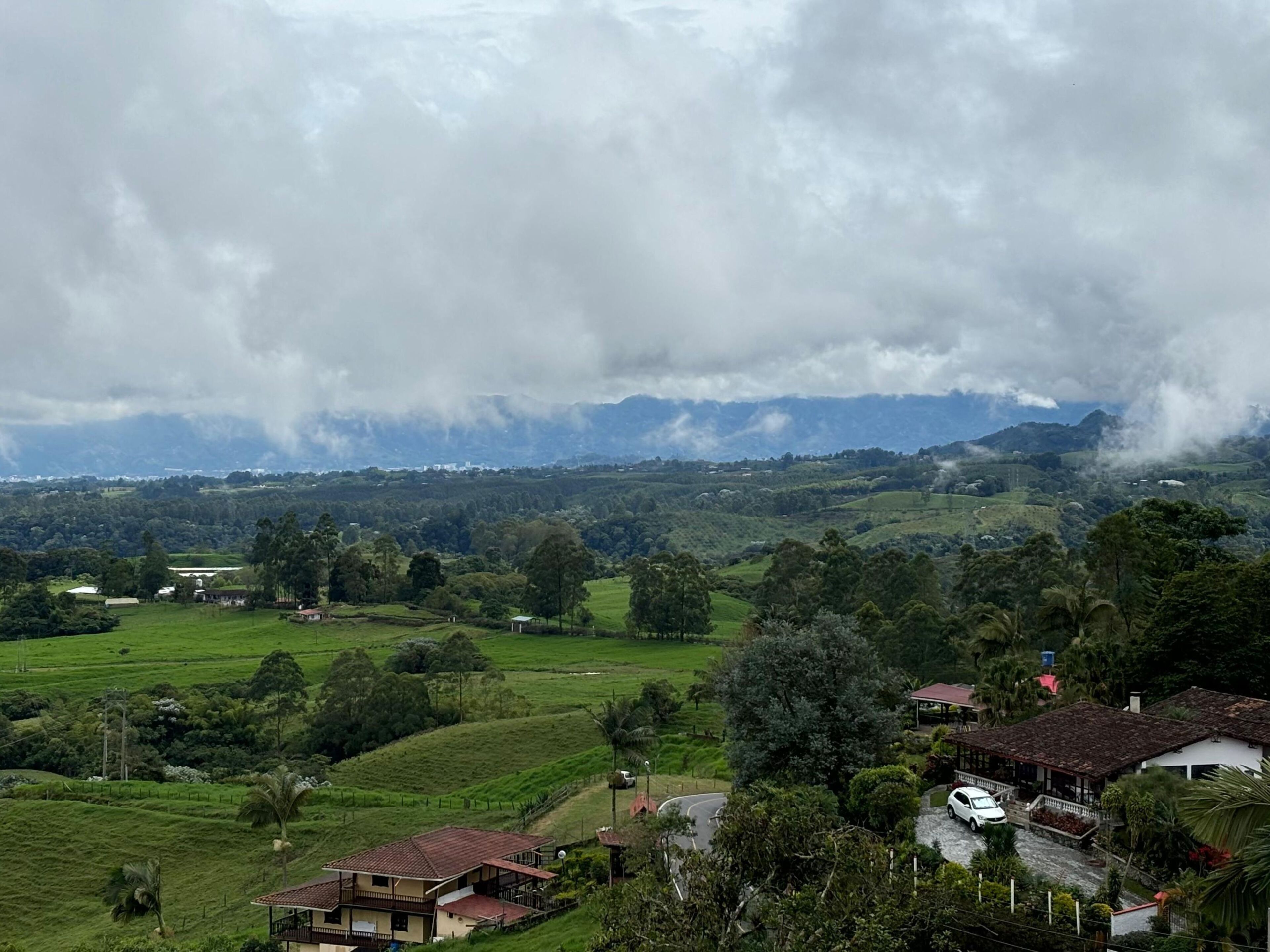 A rural landscape with rolling hills, scattered houses, and a road.